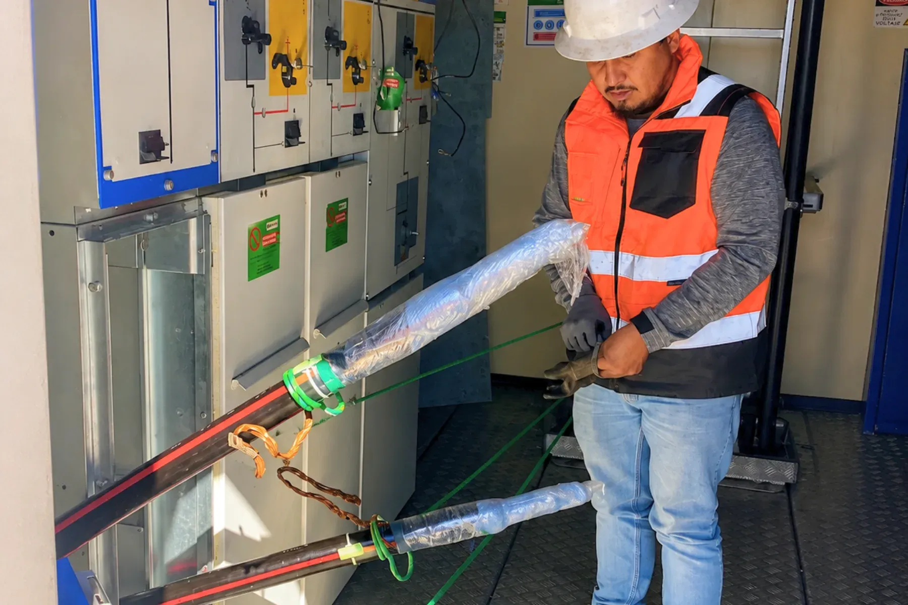 Técnico con casco y chaleco reflejante manipulando cables de potencia de media tensión con sus terminales preparadas, conectados a una celda de media tensión para pruebas