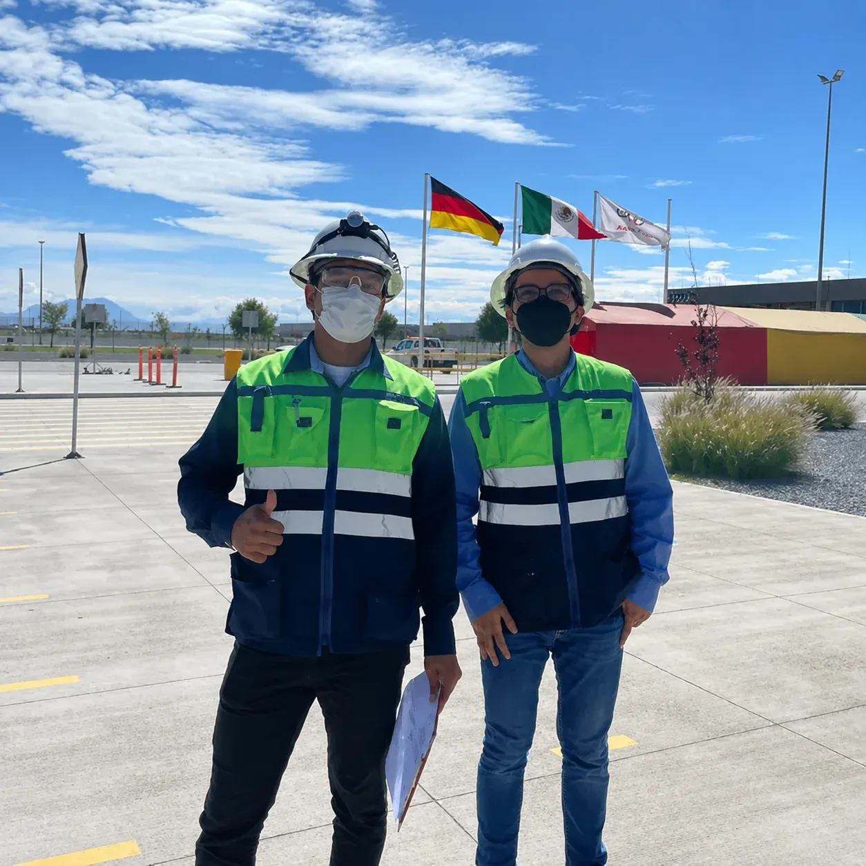 Dos ingenieros de iT Power Systems con casco, careta y chaleco reflejante en el acceso a una planta automotriz donde ejecutan trabajos eléctricos