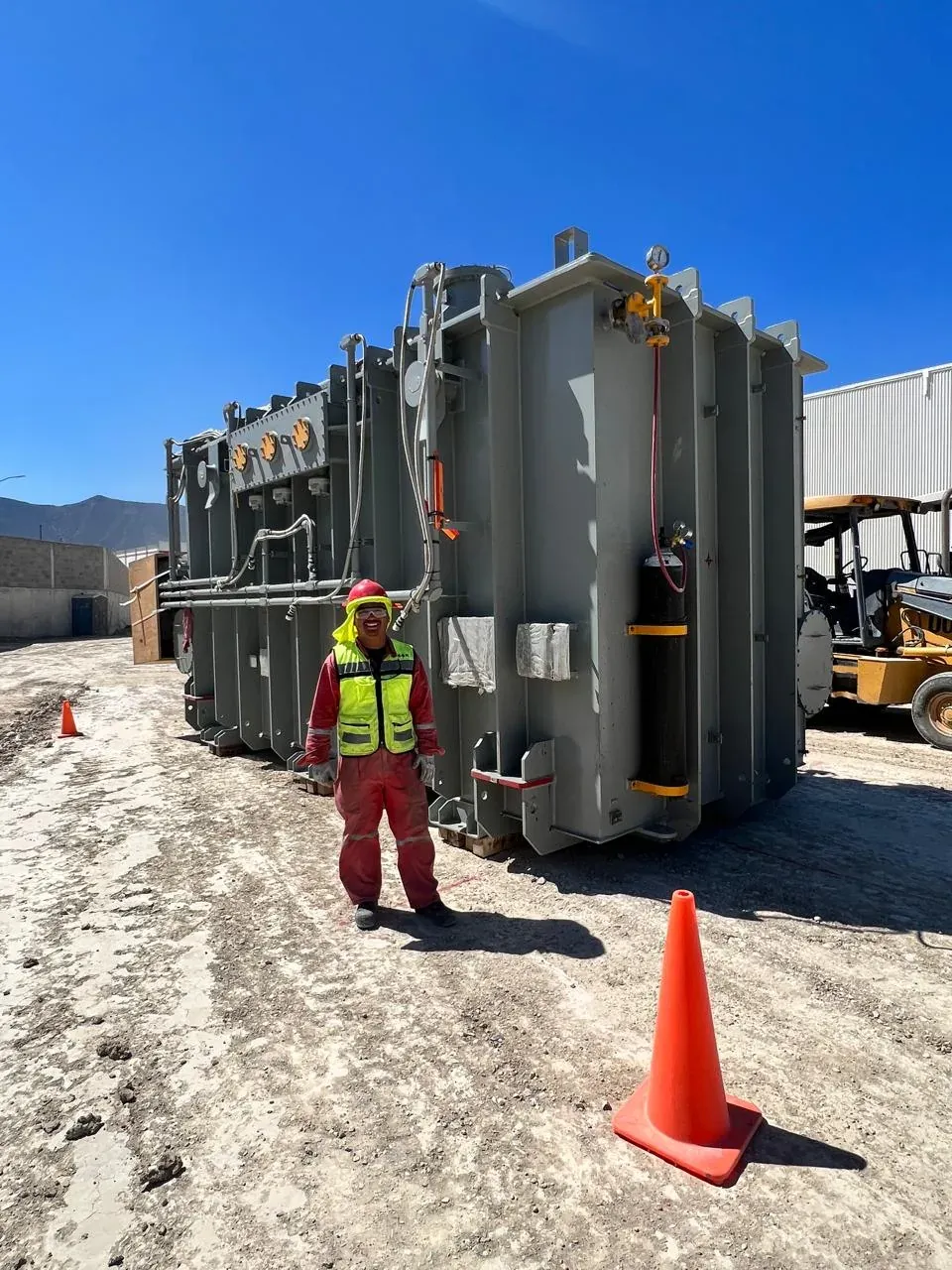 Técnico de iT Power Systems con overol y chaleco reflejante junto a un transformador de potencia recién montado a la intemperie en una planta industrial
