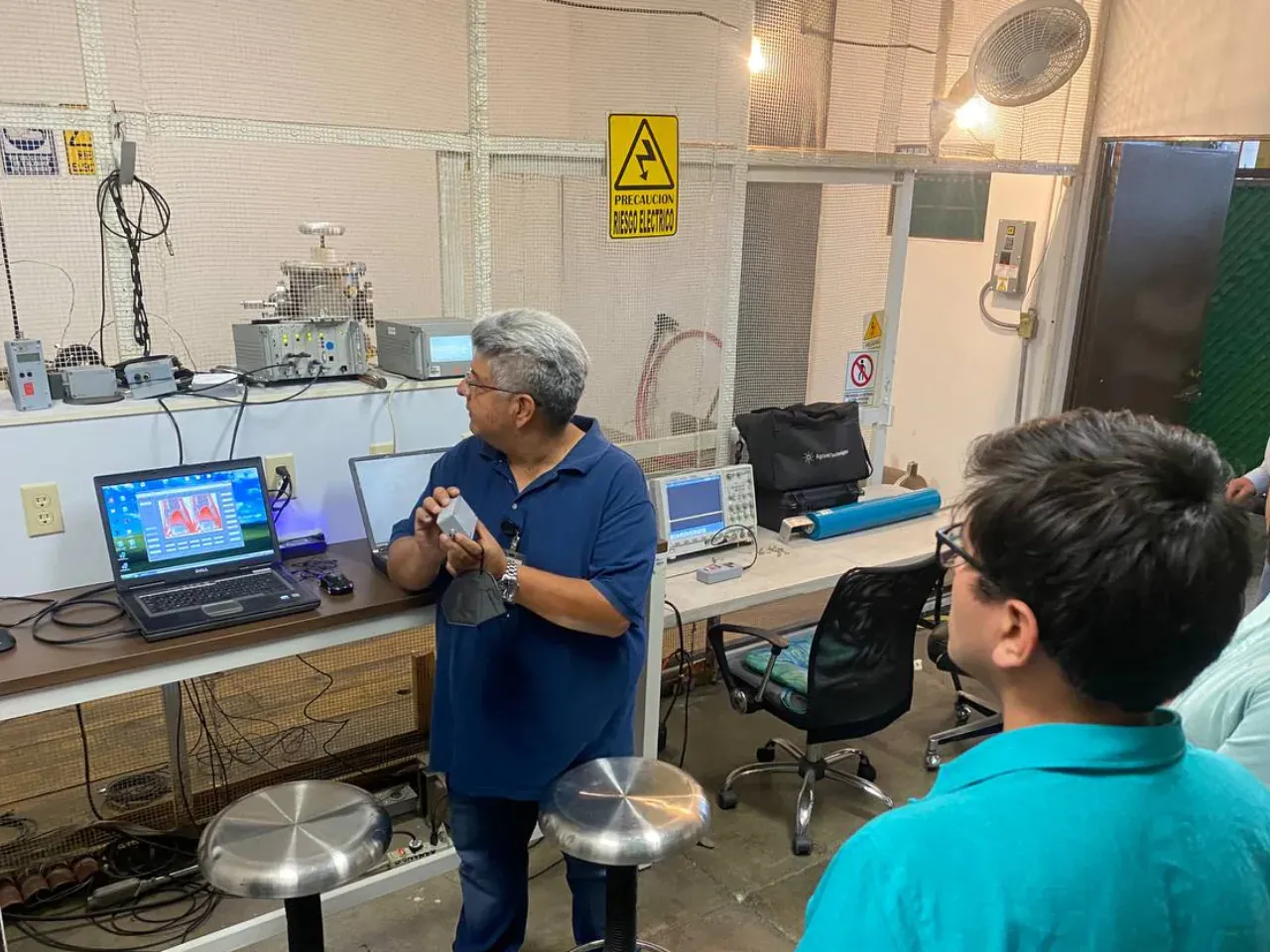Ingeniero de iT Power Systems explicando resultados de prueba frente a un banco de laboratorio con osciloscopio, fuente de alta tensión y una laptop que muestra formas de onda