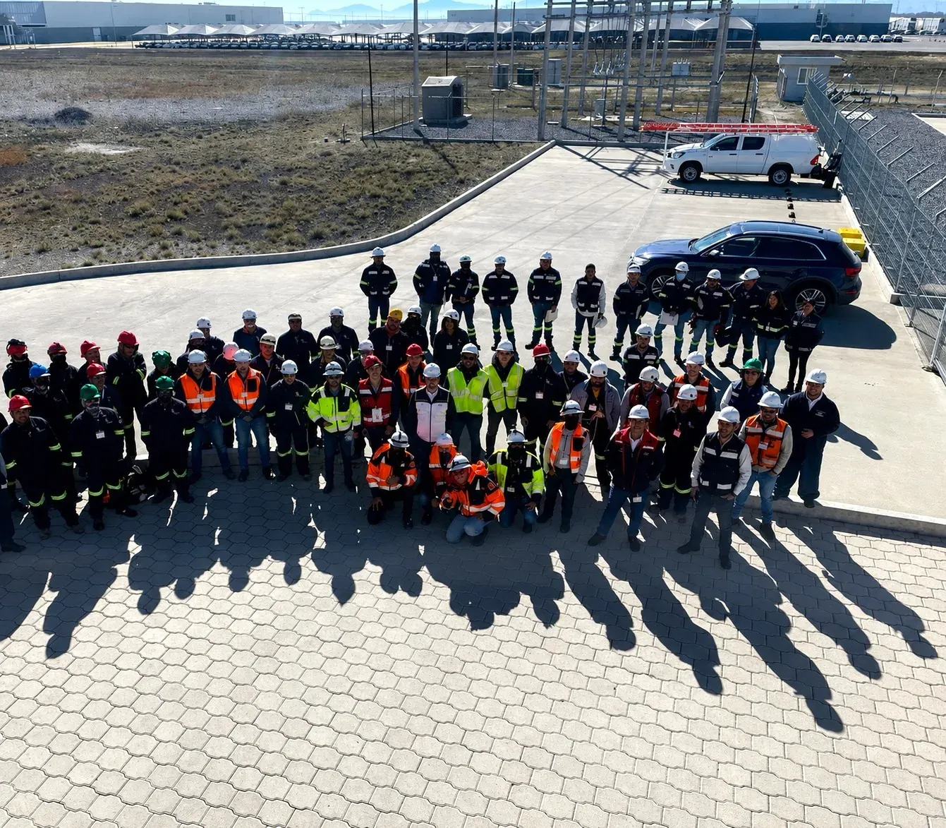 Fotografía grupal del equipo completo de iT Power Systems, con casco y chaleco reflejante, posando frente a una subestación en una planta industrial