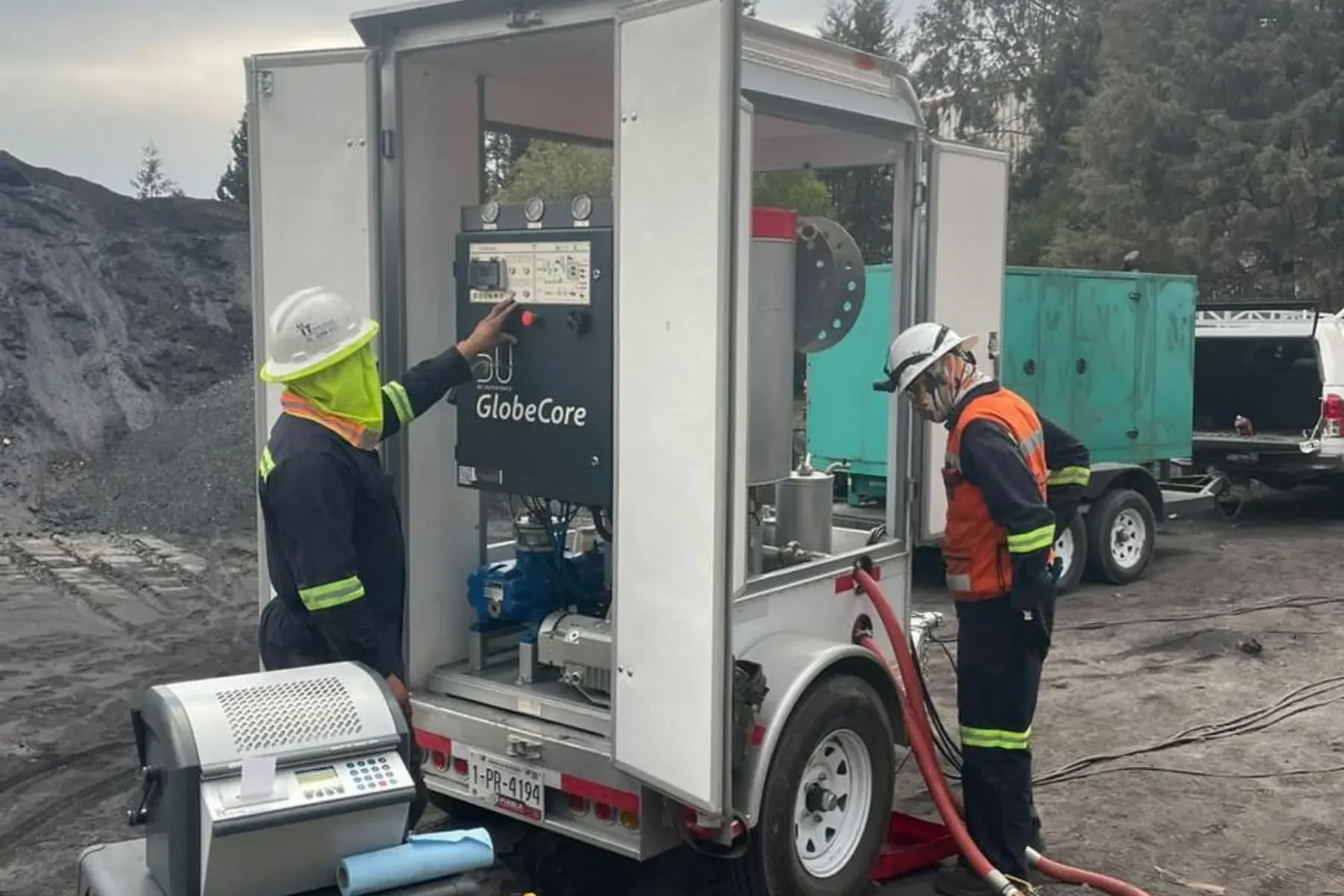 Dos técnicos de iT Power Systems operando en sitio una planta de termovacío GlobeCore para filtrar y desgasificar el aceite aislante, con un medidor portátil de rigidez dieléctrica en primer plano