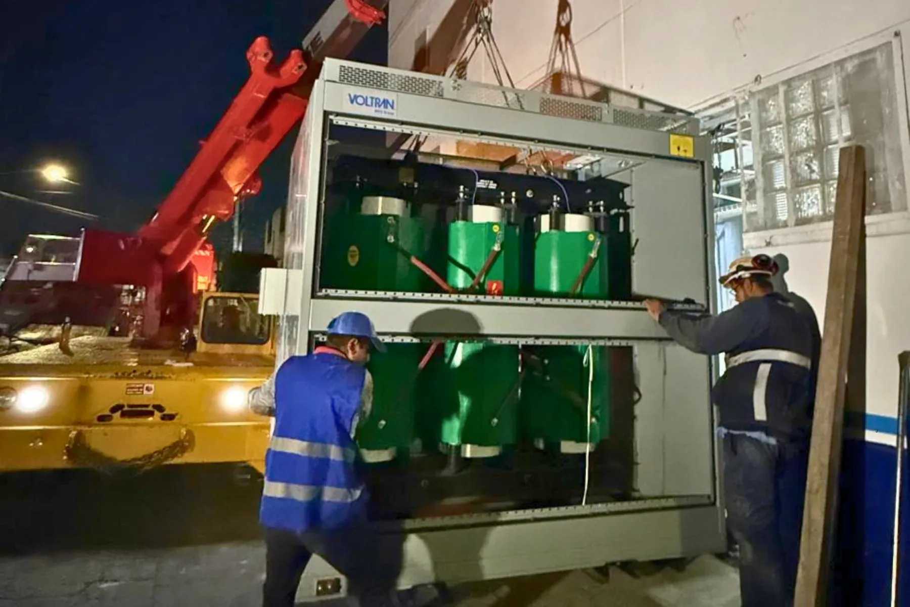 Dos técnicos de iT Power Systems maniobrando con grúa un transformador seco encapsulado dentro de su gabinete para instalarlo en una nave industrial, en trabajo nocturno
