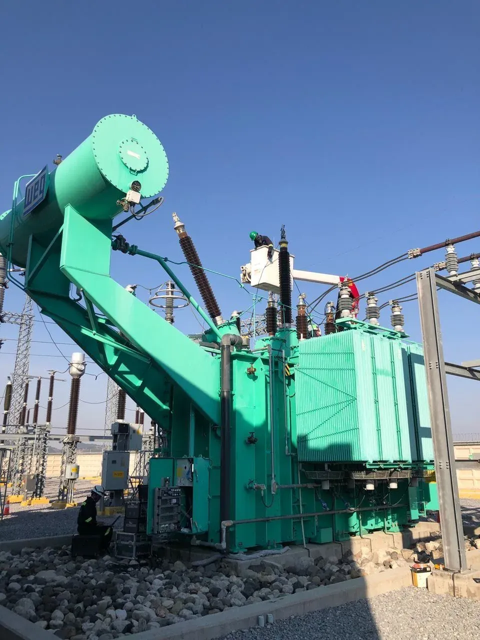 Cuadrilla de iT Power Systems dando mantenimiento a un transformador de potencia en una subestación, con un operario en canastilla trabajando sobre las boquillas de alta tensión y equipo de prueba en el suelo