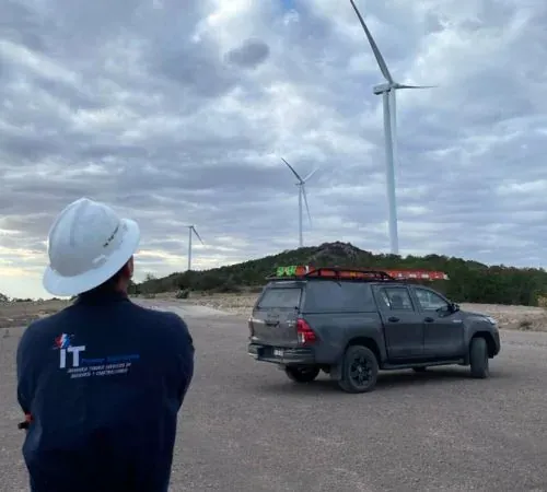 Técnico de iT Power Systems con casco blanco observando los aerogeneradores de un parque eólico, junto a la camioneta de trabajo con escalera en el techo