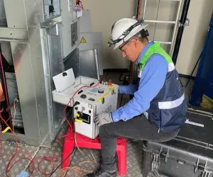Técnico de iT Power Systems sentado frente a una celda de media tensión, operando un equipo de prueba conectado con cables rojos al interior del tablero