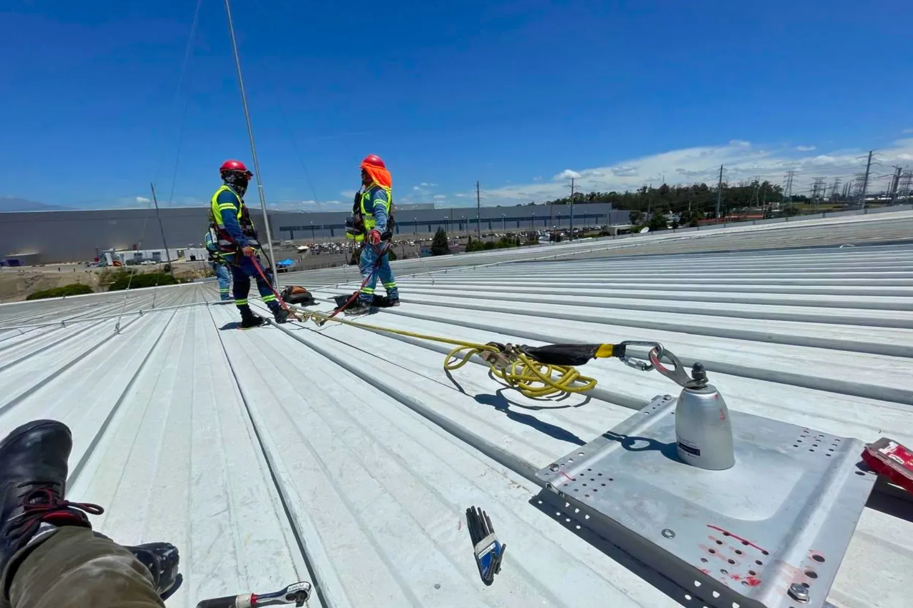 Dos técnicos de iT Power Systems con arnés de protección contra caídas instalando los mástiles de un sistema de pararrayos sobre la cubierta metálica de una nave industrial
