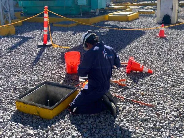 Técnico de iT Power Systems revisando la conexión de puesta a tierra en un registro abierto dentro del patio de grava de una subestación