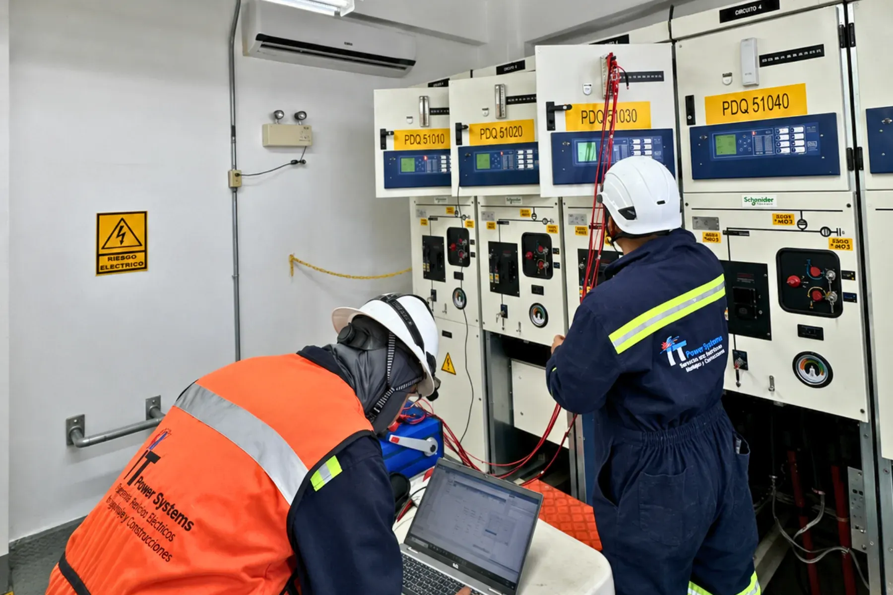 Dos técnicos de iT Power Systems probando los relevadores de protección de una línea de celdas de media tensión, con laptop y equipo de inyección conectado, en una subestación