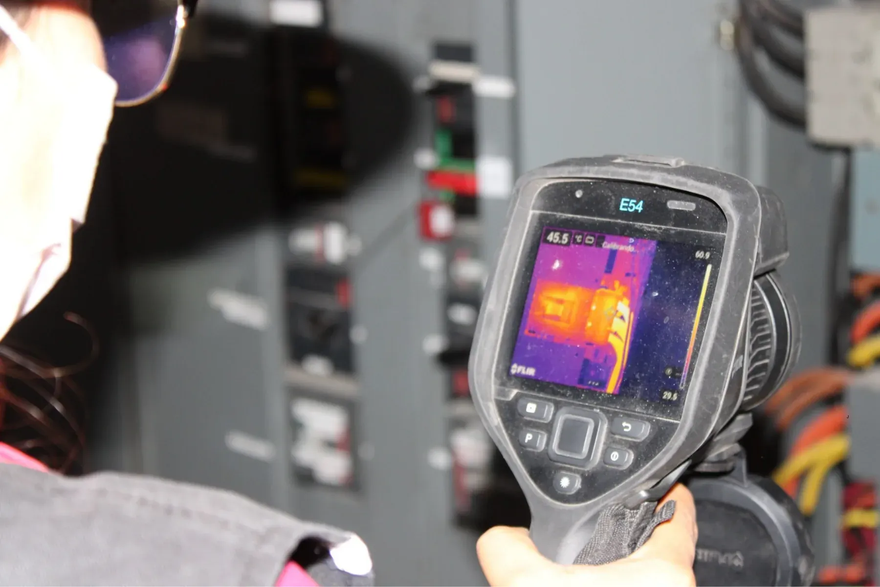 Técnico de iT Power Systems inspeccionando un tablero eléctrico con una cámara termográfica FLIR, con el termograma en pantalla mostrando un punto caliente