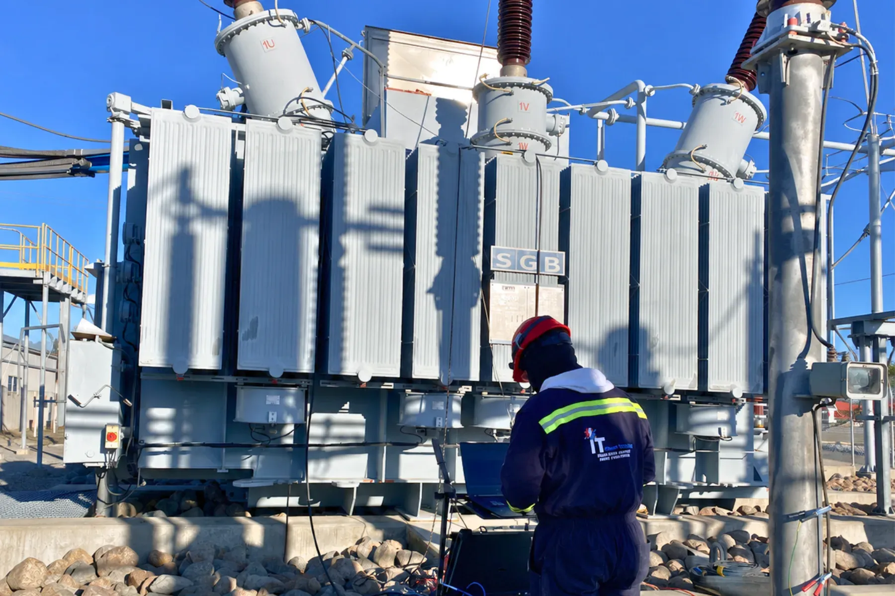 Técnico de iT Power Systems con equipo de prueba y laptop conectados a un transformador de potencia en el patio de una subestación de intemperie, realizando pruebas eléctricas